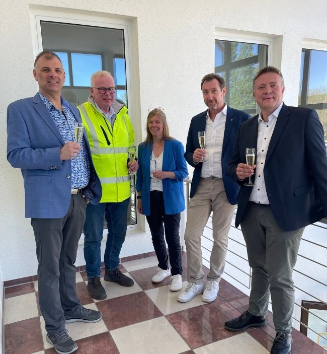Gruppenfoto beim Besuch des zukünftigen Standorts der Süd-Eis GmbH & Co. KG in Bad Iburg. Mehrere Personen stehen mit Sektgläsern in einem modernisierten Gebäude der ehemaligen Teutoburger Wurstfabrik im Gewerbegebiet Sentrup.